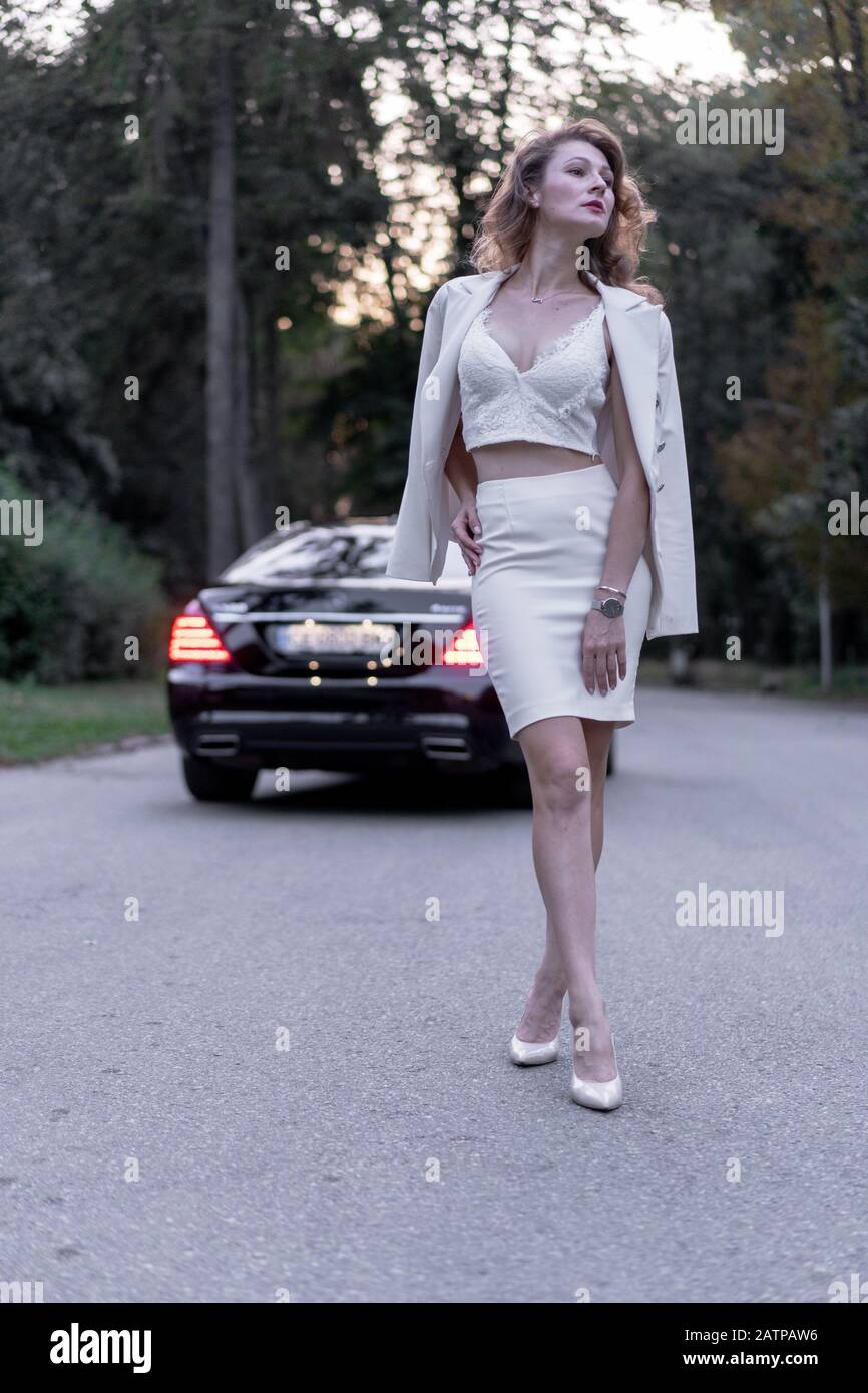 Vista a tutta lunghezza di una donna alla moda sognante in piedi vicino all'auto. Foto Stock Vista a tutta lunghezza di una donna alla moda sognante in piedi vicino all'auto. Foto Stock