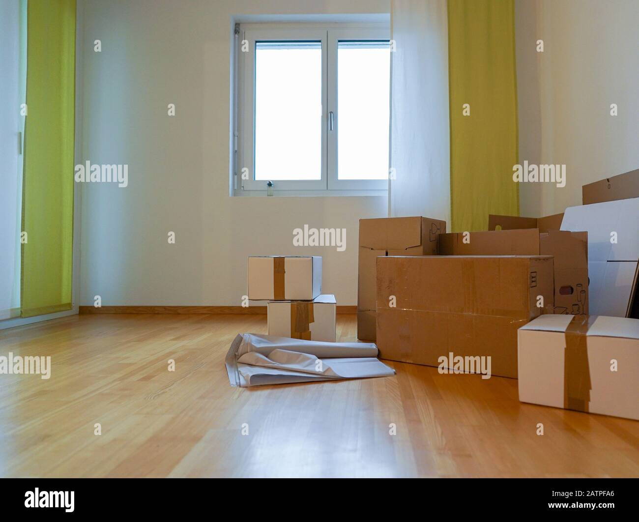 Vista di scatole e materiali mobili in un soggiorno vuoto con pavimento in legno e pareti bianche Foto Stock