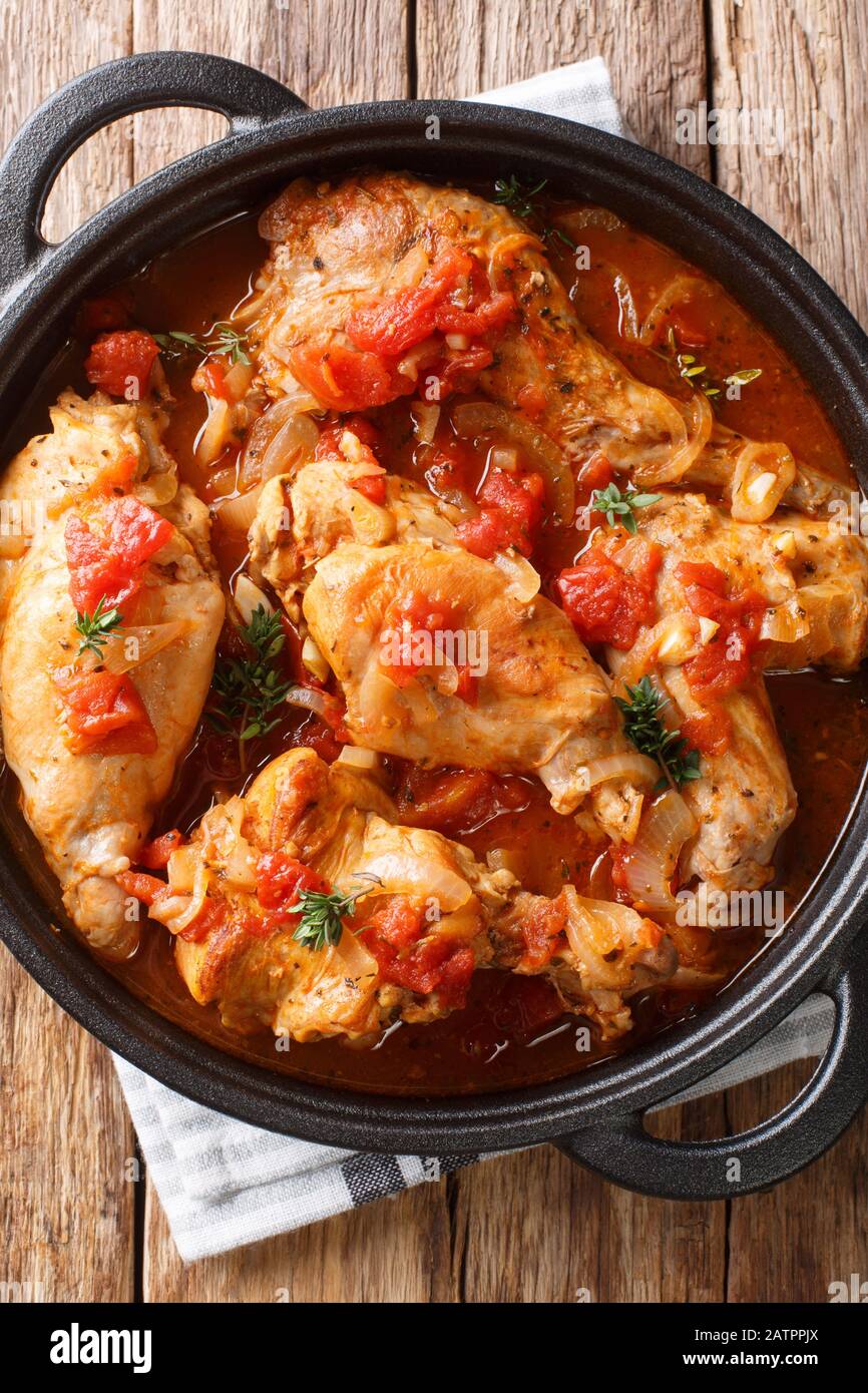 Dieta carne di coniglio stufato in salsa di pomodoro con vino bianco e erbe primo piano in una padella sul tavolo. Vista dall'alto verticale Foto Stock
