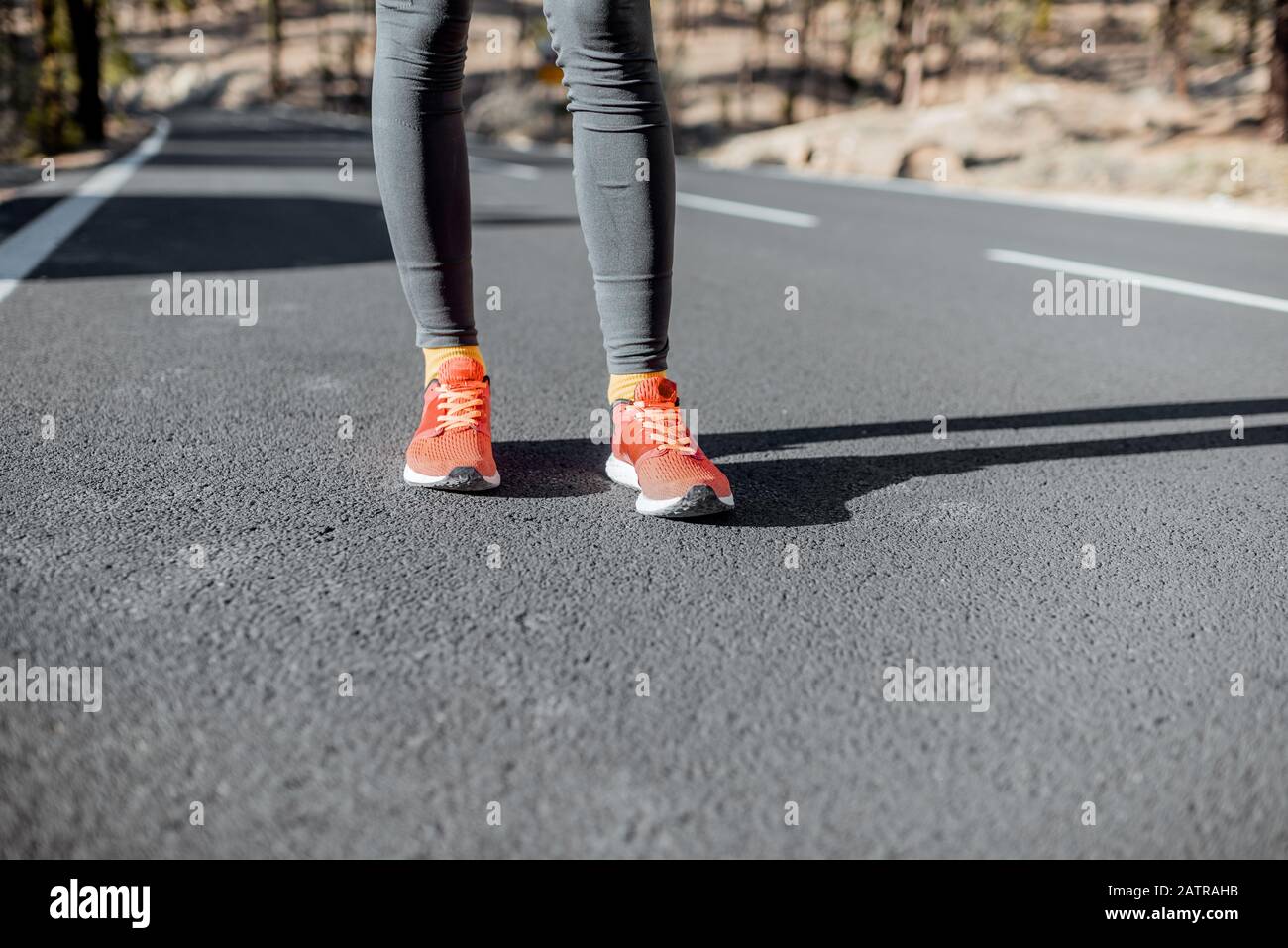 Donna sportiva in scarpe da running in piedi sulla strada di montagna asfaltata, da vicino sulle sneakers Foto Stock