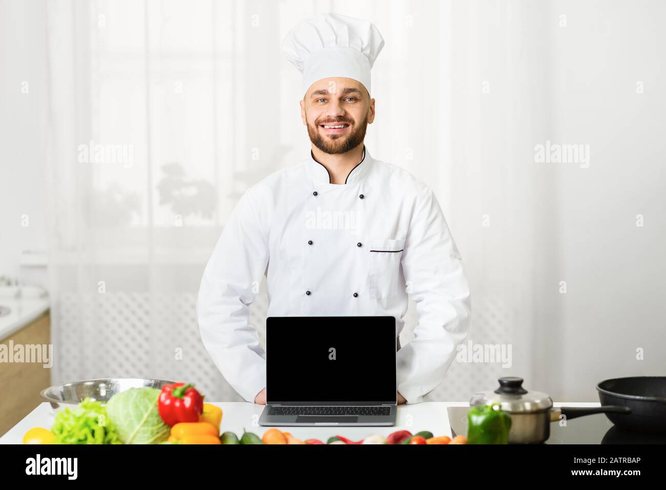 Chef Maschile Che Mostra Lo Schermo Del Computer Portatile In Cucina, Mockup Foto Stock