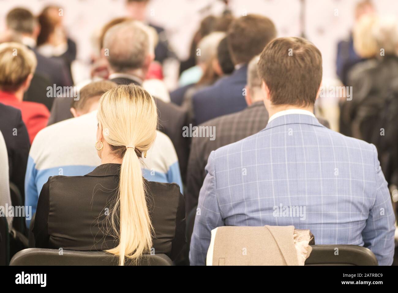 Uomo d'affari e donna bionda con capelli lunghi e persone che ascoltano la conferenza o la formazione nella sala Foto Stock