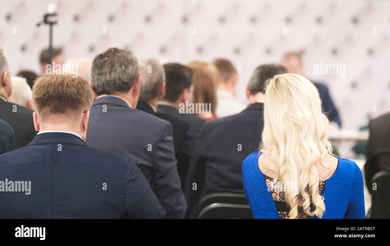 Uomo d'affari e donna bionda con capelli lunghi e persone che ascoltano la conferenza o la formazione nella sala Foto Stock