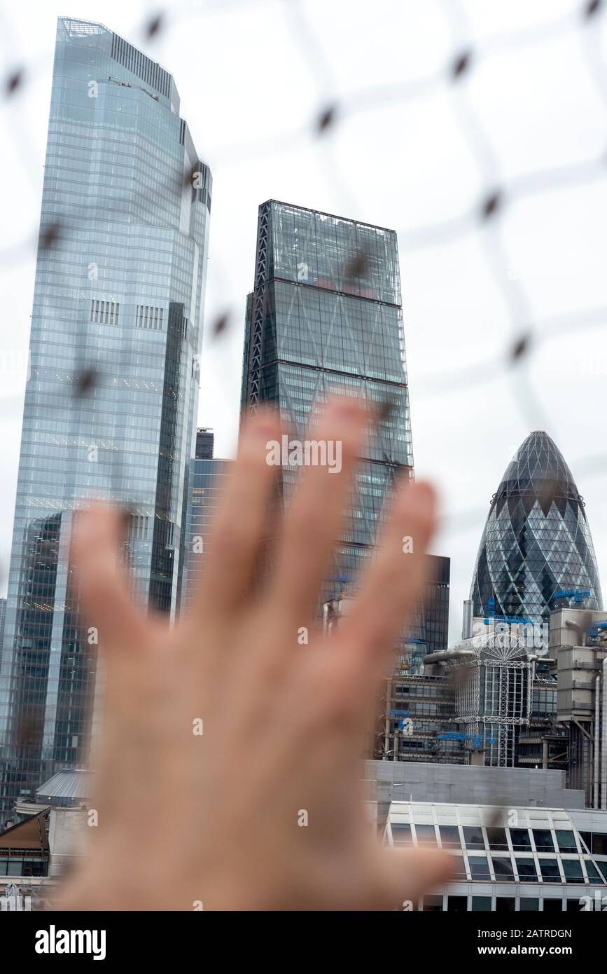 Vista insolita degli edifici della City of London e della recinzione in rete metallica defocalizzata come concetto di ansia urbana e incertezza Foto Stock