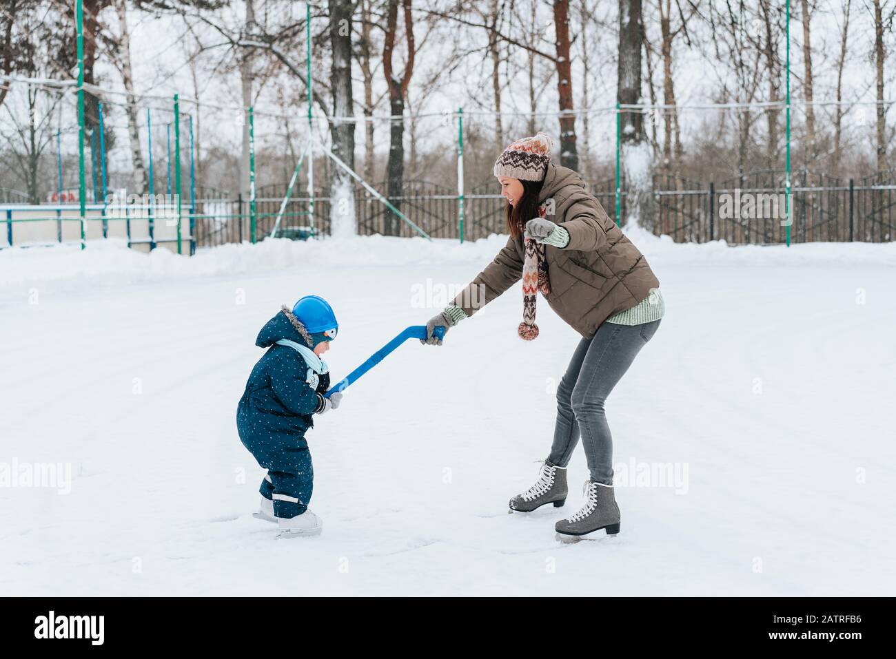 Ragazzino divertente con la sua madre che pattina nel parco. Gioca a hockey su ghiaccio con bastone e obiettivo. All'Aperto. Sport invernali Foto Stock