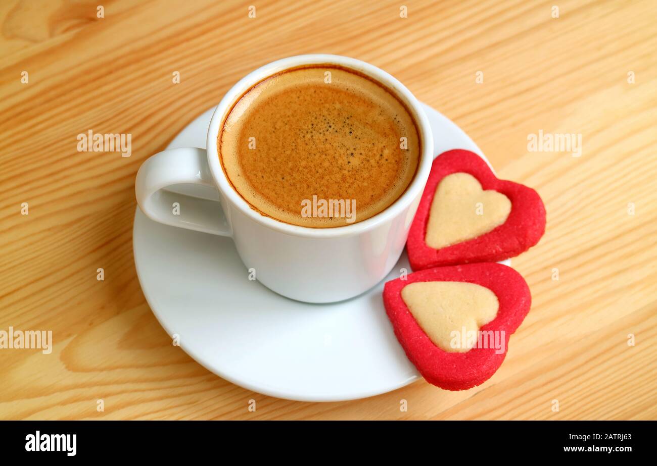 Una tazza di caffè espresso con Un Paio di biscotti rossi A Forma Di Cuore su tavola in legno per San Valentino Foto Stock