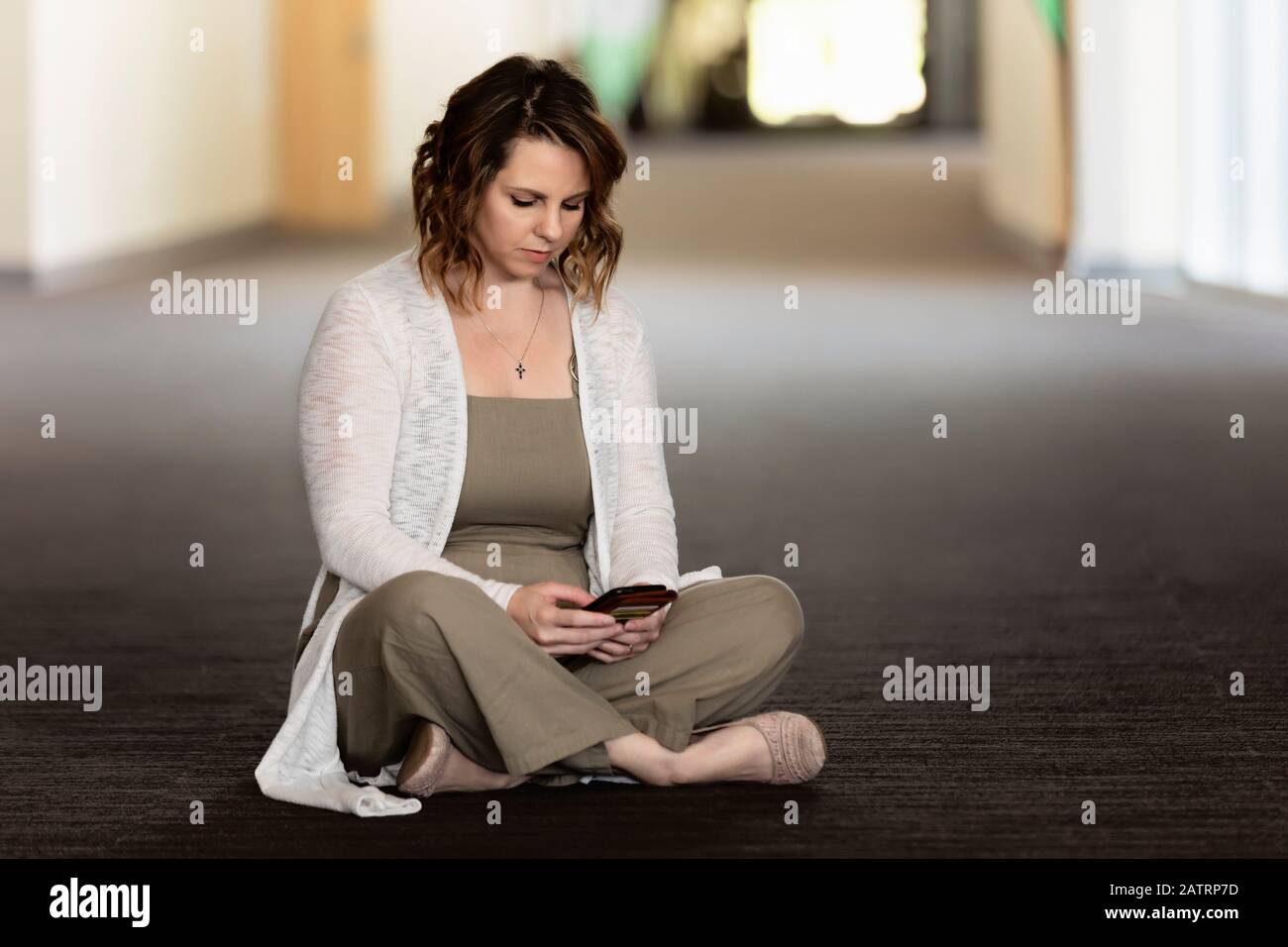 Una donna matura che si siede nel mezzo di un corridoio sul suo posto di lavoro, controllando il suo smartphone e godendo la solitudine: Edmonton, Alberta, Canada Foto Stock