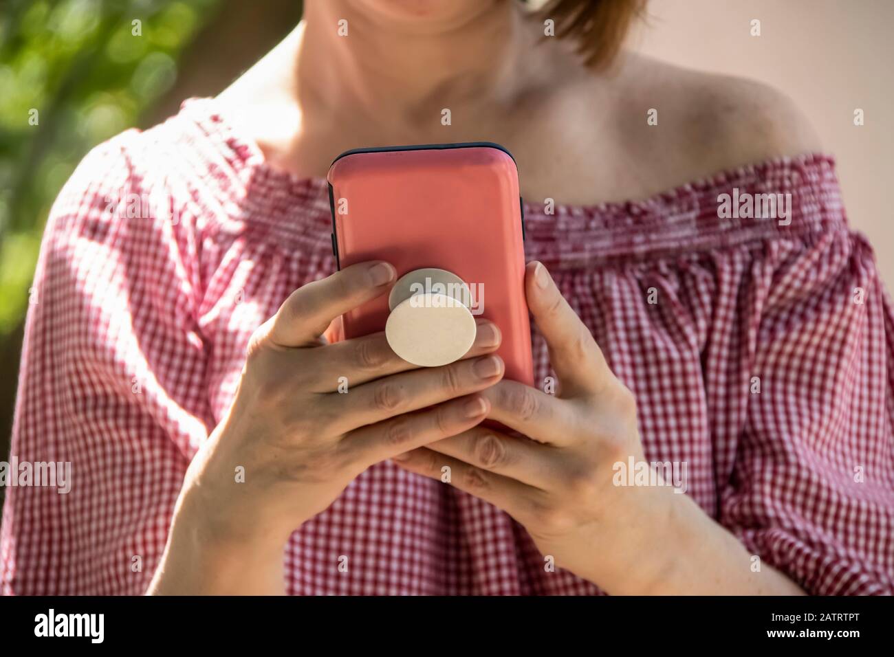 Primo piano di donna che tiene e legge da un telefono cellulare in una custodia rosa con impugnatura sul retro - off blusa spalla e capelli corti - fuoco selettivo Foto Stock