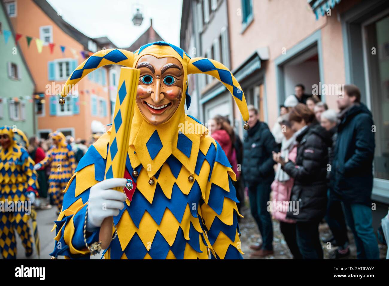 Bajass da Waldkirch - figura sciocco in veste giallo-blu mostra un oggetto tradizionale, durante la sfilata di carnevale a Staufen, Germania meridionale Foto Stock
