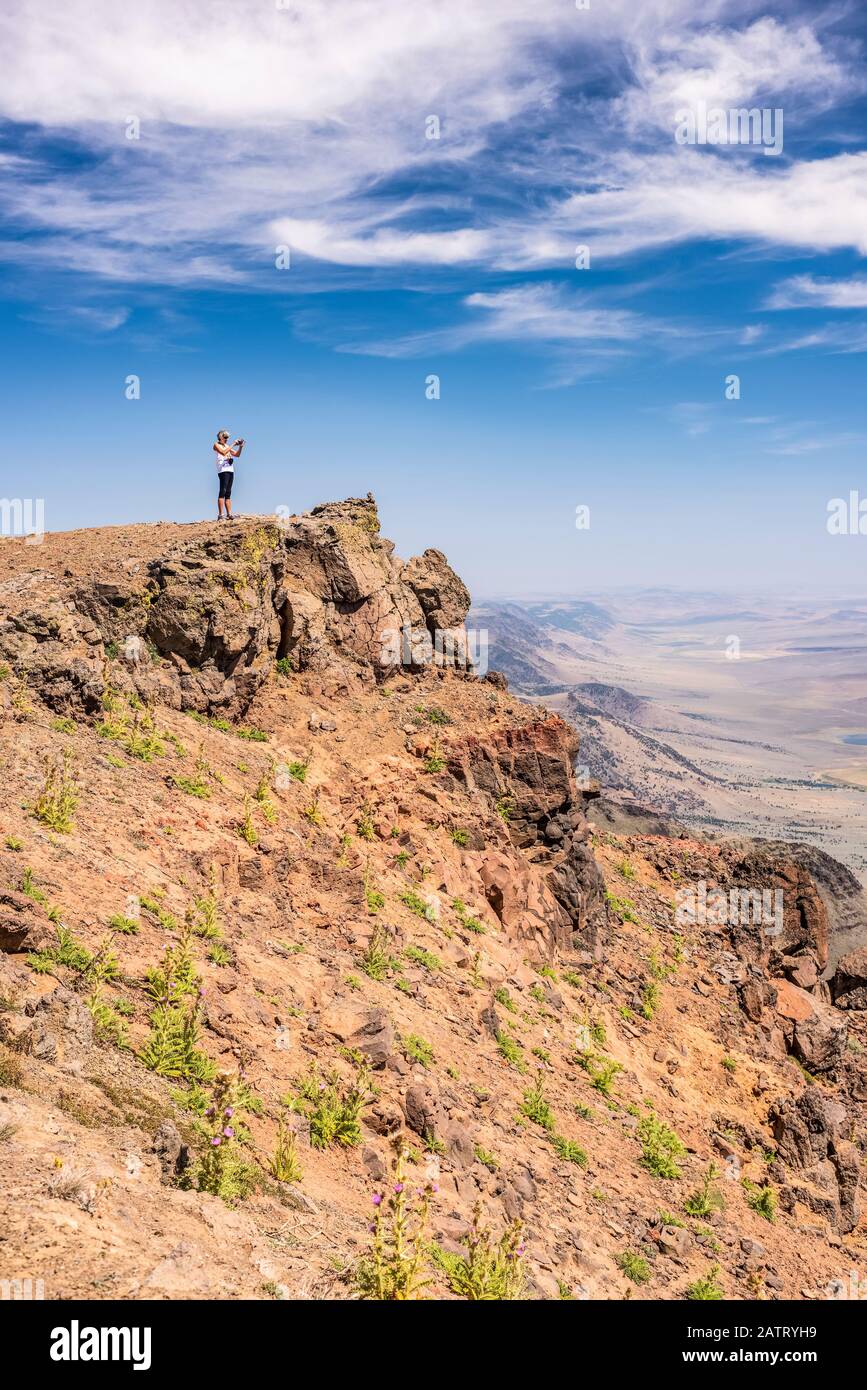 Una donna che guarda attraverso il deserto dell'Alvord da una scogliera a bordo di Steens Mountain, Oregon sud-orientale; Frenchglen, Oregon, Stati Uniti d'America Foto Stock