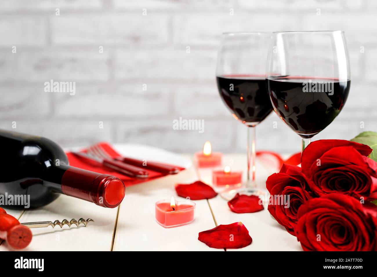 Cena di un giorno in San Valentino. Due bicchieri di vino, bottiglia di vino, cavatappi, rose rosse, piastra e candele brucianti su un tavolo di legno bianco. Selettivo fo Foto Stock