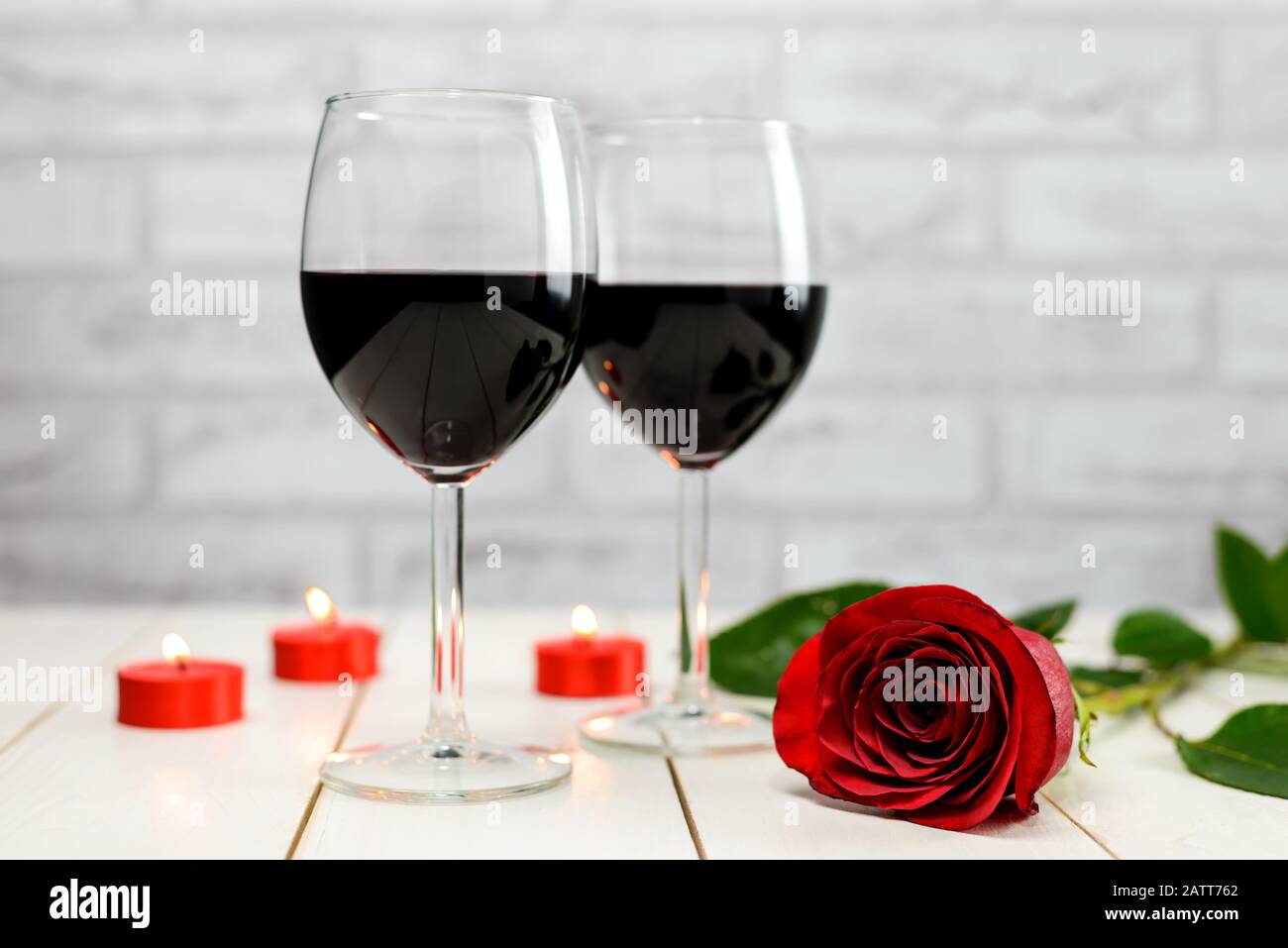 Concetto di San Valentino. Due bicchieri di vino, rosa rossa e candele accese su un tavolo di legno bianco. Foto Stock