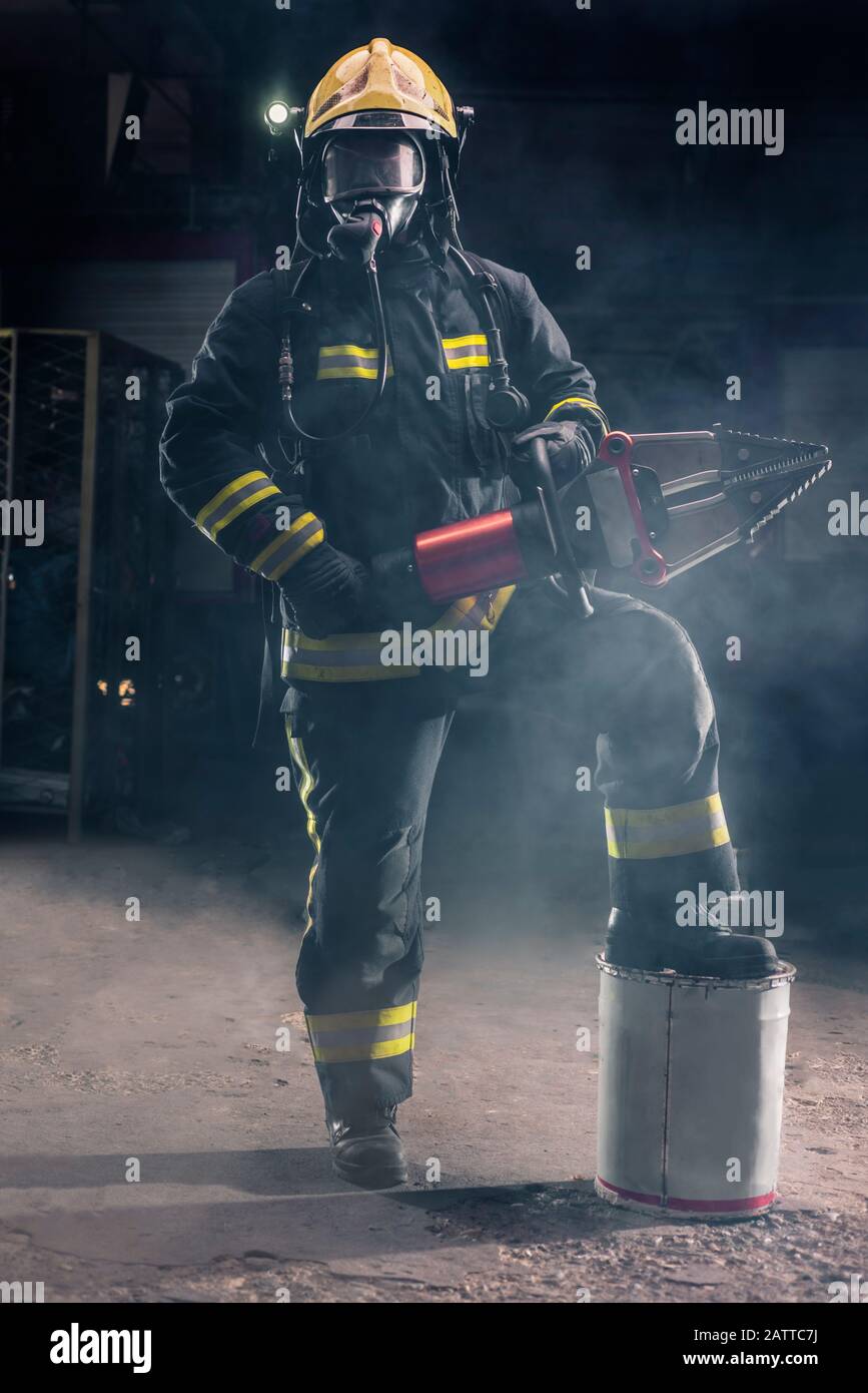 Ritratto di un coraggioso pompiere in piedi sicuro indossando attrezzatura di protezione completa, giradischi e casco. Sfondo scuro con fumo e luce blu. Foto Stock