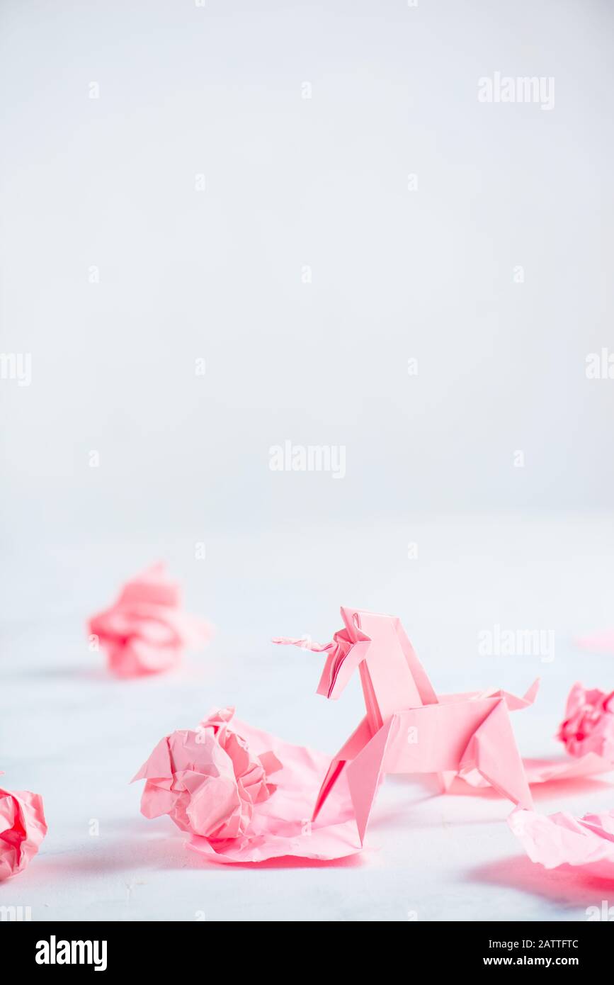 Unicorno di origami rosa con palline di carta sbriciolate. Processo creativo è scrittura, sfondo chiaro Foto Stock