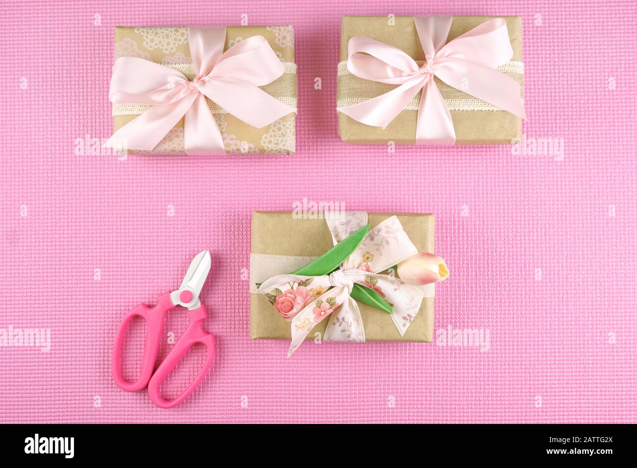 Regali avvolti in carta kraft e nastri rosa overhead laici piatto per la Festa della mamma, festa di compleanno o il giorno di San Valentino celebrazioni. Foto Stock