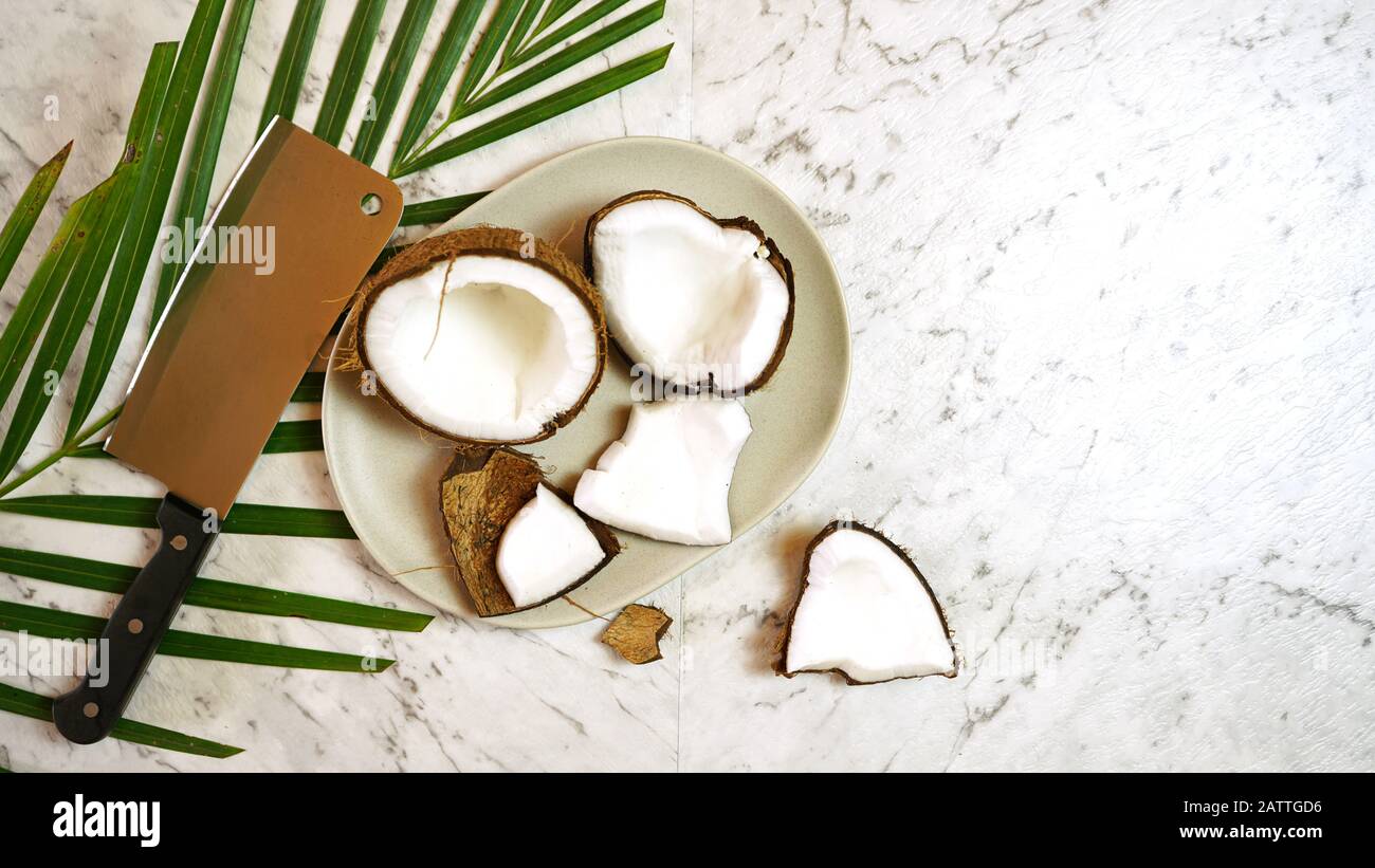 Sano nutriente noce di cocco naturale con una vasta gamma di usi dietetici e cosmetici, qui mostrato con noce di cocco tagliato in pezzi sul piano del tavolo di marmo, creati Foto Stock