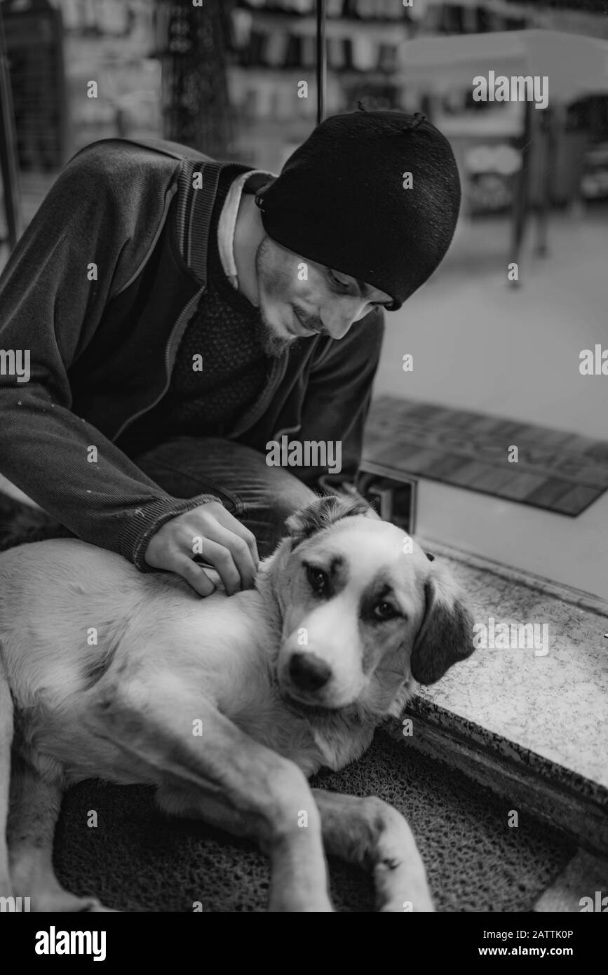 L'uomo senza tetto ama un cane vagante carino di fronte al negozio sulla strada. Concetto Di Senzatetto. Foto Stock