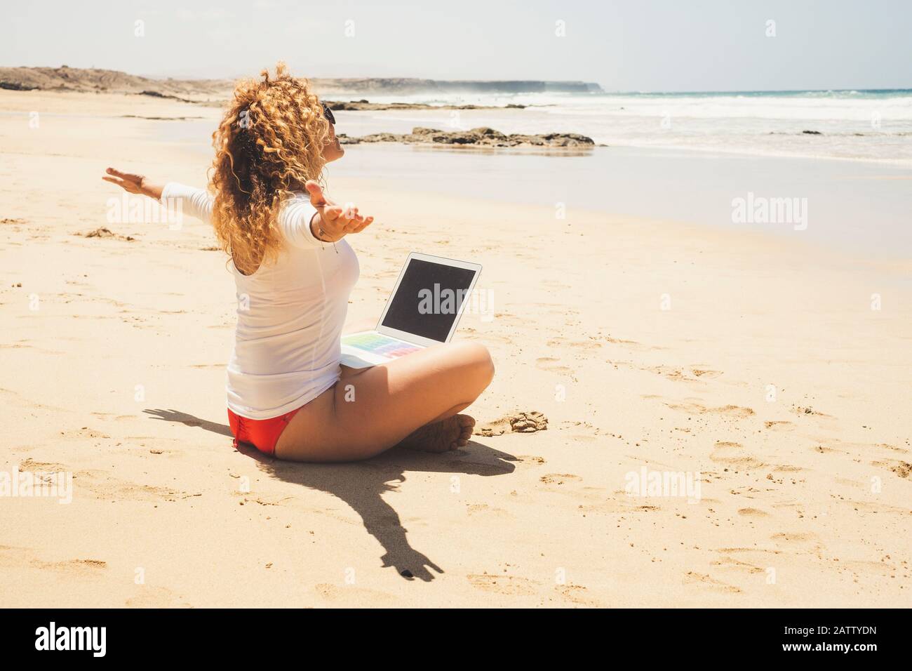 Bella donna felice e libera sedersi in spiaggia con computer portatile sulle gambe - concetto di nomade digitale e tecnologia moderna - Connected vigilia Foto Stock