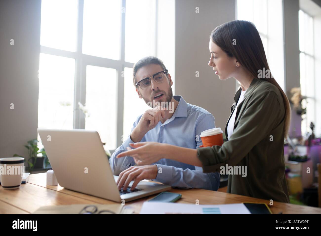 Progetto comune di impresa. Una ragazza con un bicchiere di caffè e un uomo con occhiali seduti a un tavolo vicino a un computer portatile e discutendo un progetto aziendale congiunto, Foto Stock