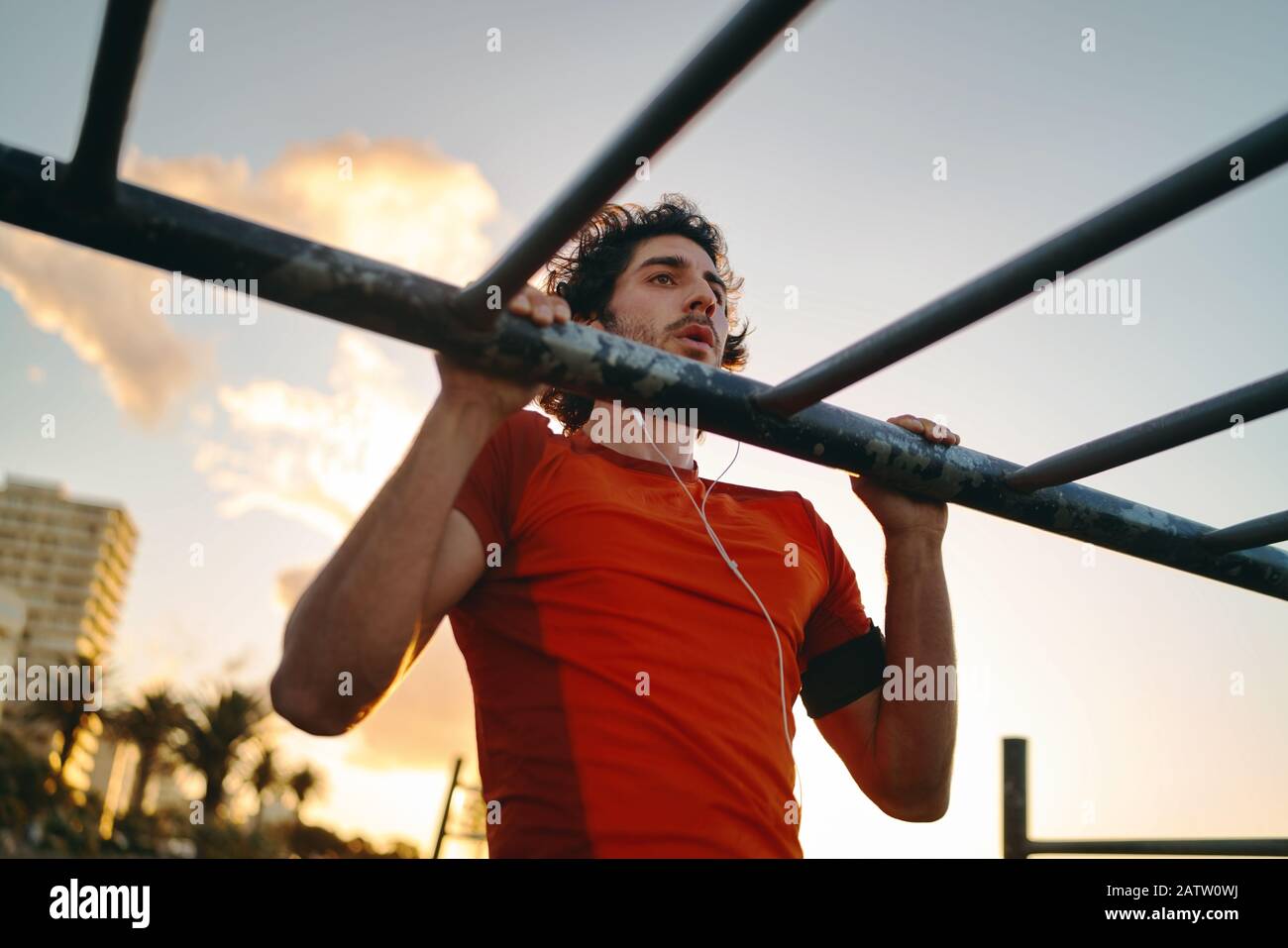 Primo piano di un giovane atleta di sesso maschile che fa esercizi al bar nel parco palestra contro il cielo - uomo che fa tirare-up all'aperto Foto Stock