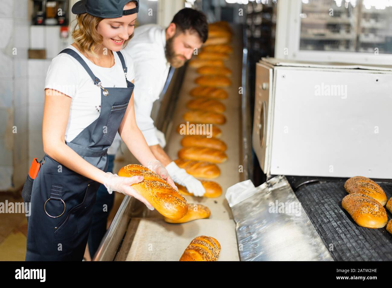Panettiera ragazza con il pane nelle sue mani sullo sfondo di una linea automatizzata in una panetteria. Produzione di pane industriale Foto Stock