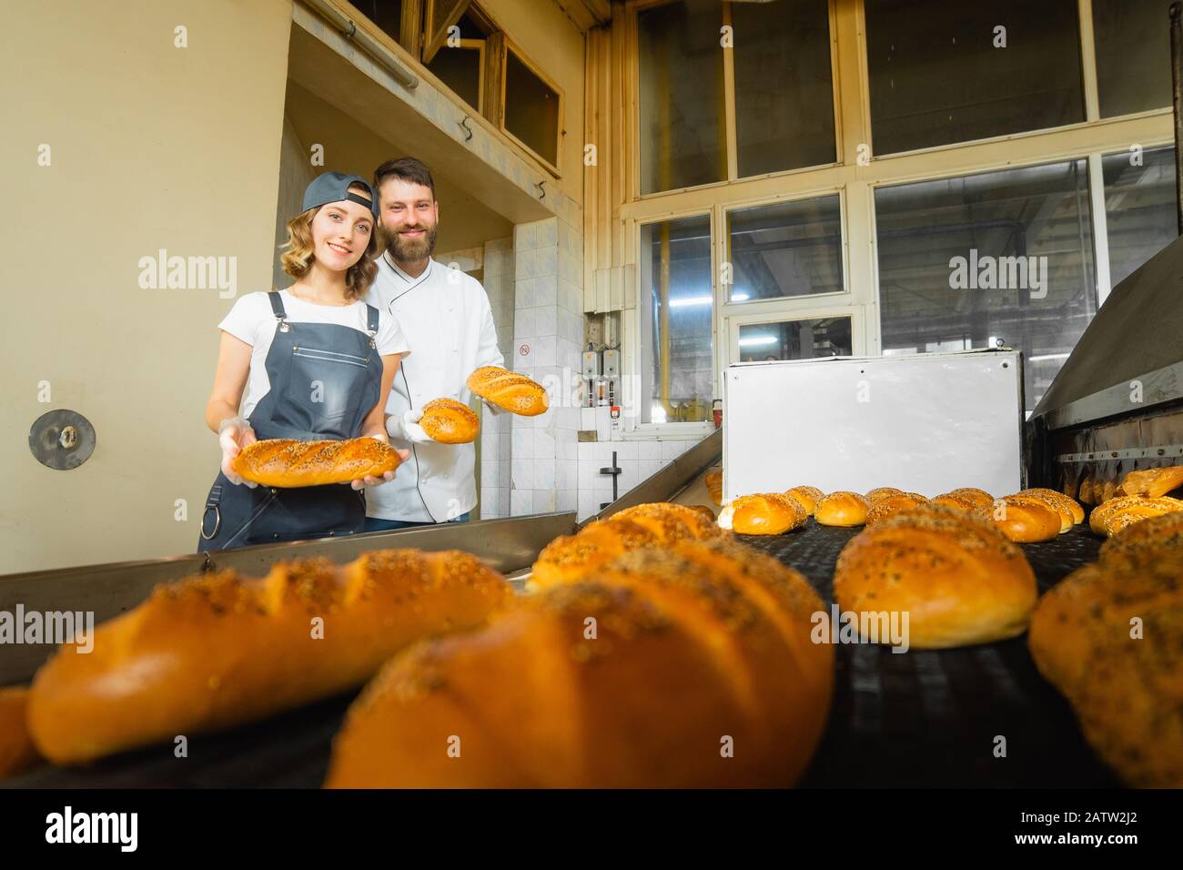 Panettieri ragazza e uomo con pane nelle loro mani sullo sfondo di un forno industriale in una panetteria. Produzione di pane industriale Foto Stock