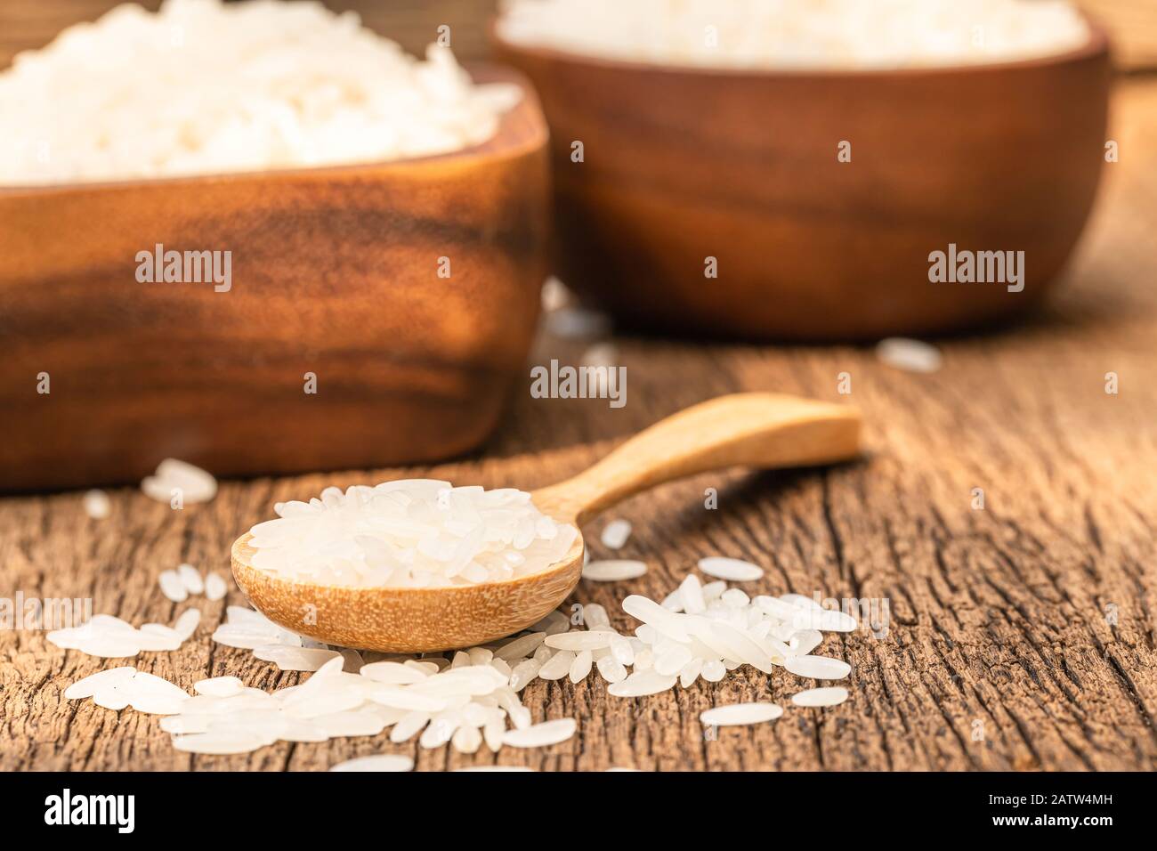 Chiudete un sacco di riso a grani lunghi su un cucchiaio di legno su sfondo di legno. Foto Stock