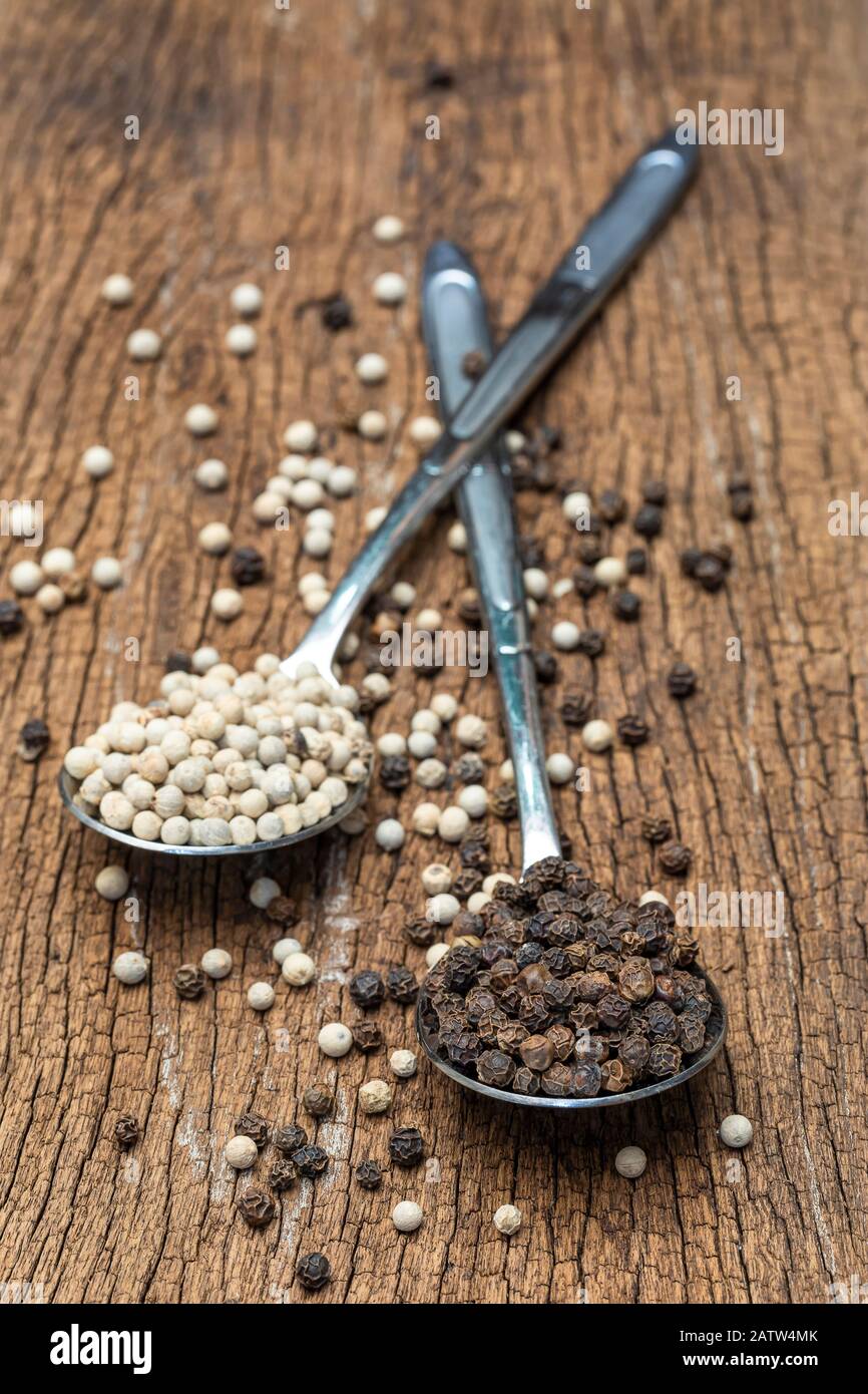 Primo piano di peperoni bianchi e peperoni neri su cucchiaio su fondo di legno. Foto Stock