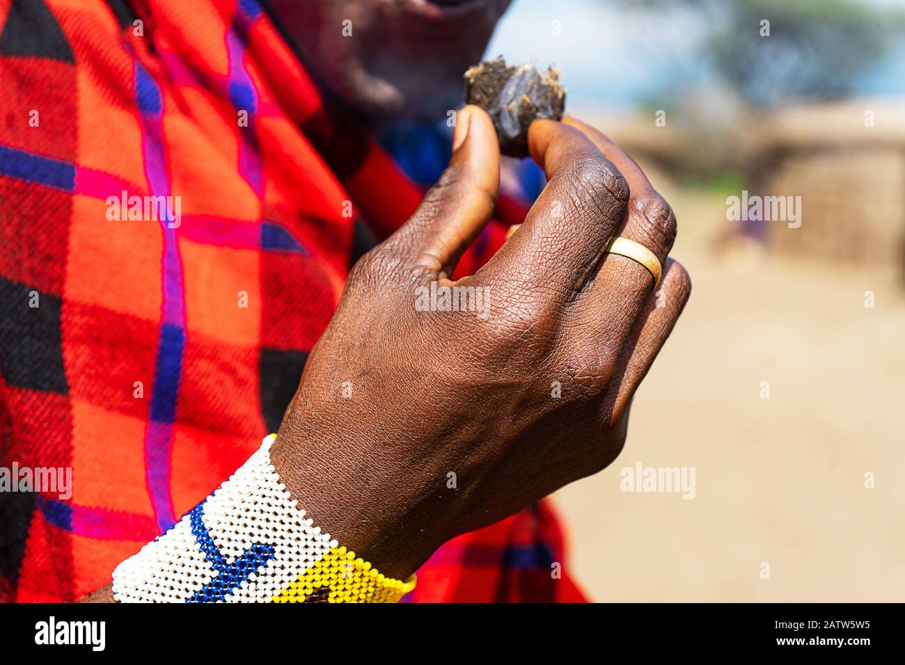 Uomo africano che tiene in mano una torta smoldering con bracciale colorato. Tanzania, Africa. Foto Stock