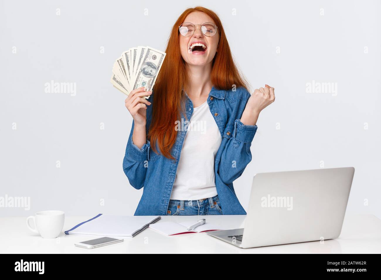 La ragazza sollevata e felice diventa ricca dopo aver fatto molto, scuotendo le mani, pugno pompa dicendo sì e alzando testa in su cielo felice, tenendo i soldi grandi Foto Stock