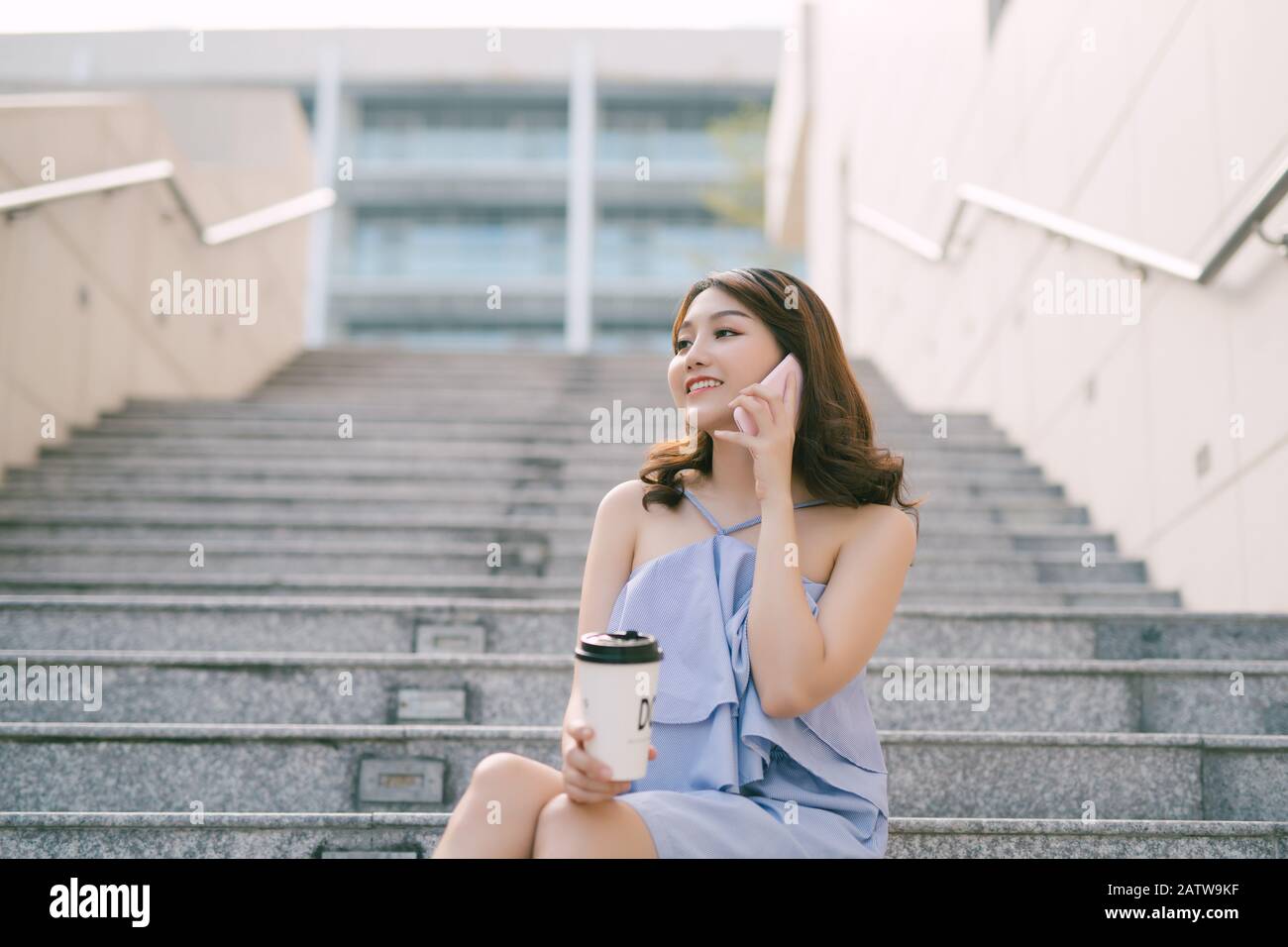 Allegro giovane ragazza asiatica parlando al telefono mentre è seduto alla scala esterna. Stile di vita urbano della ragazza. Foto Stock