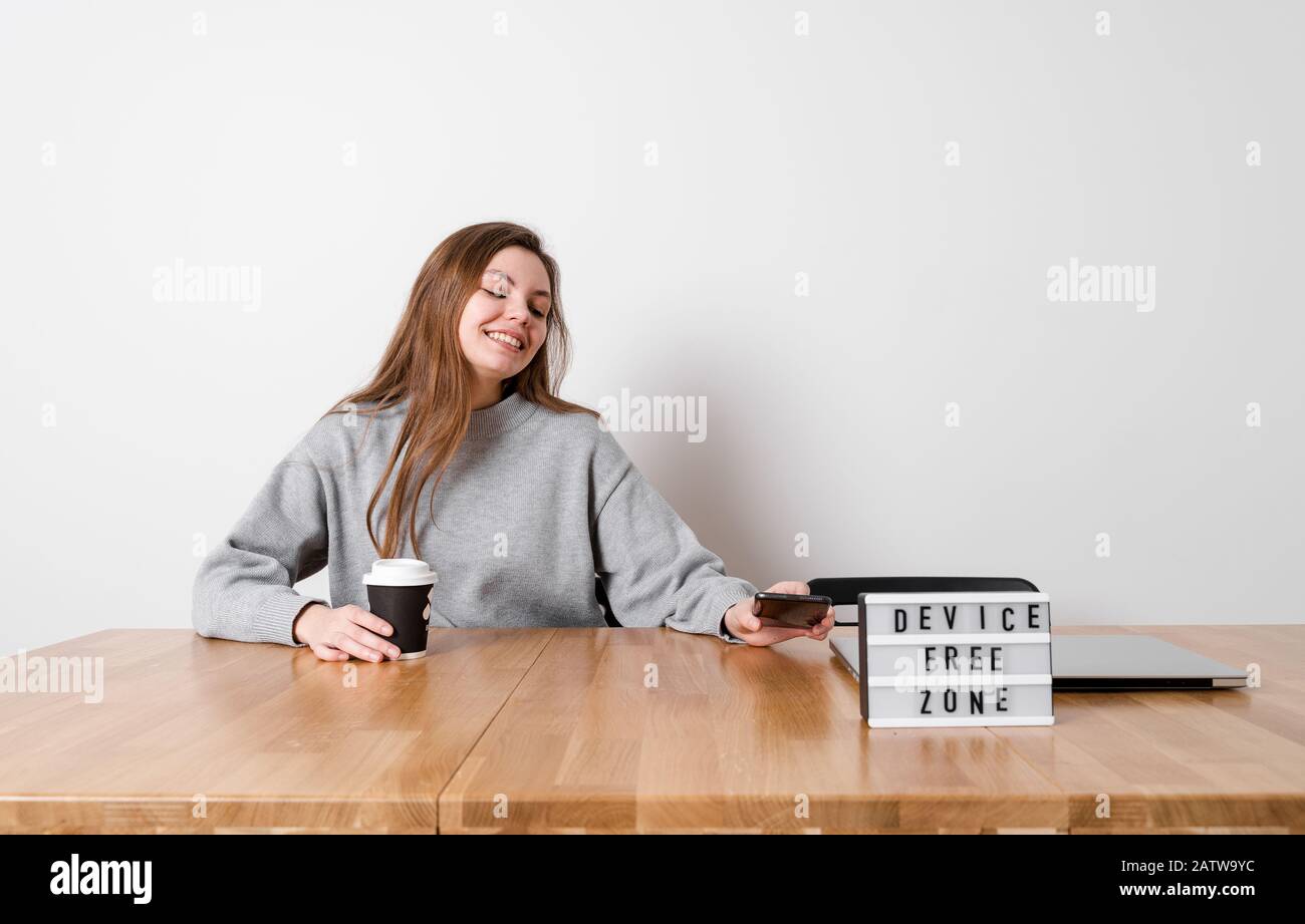 Felice ragazza seduta rilassato al tavolo con segno dispositivo zona libera. Concetto di detox digitale Foto Stock