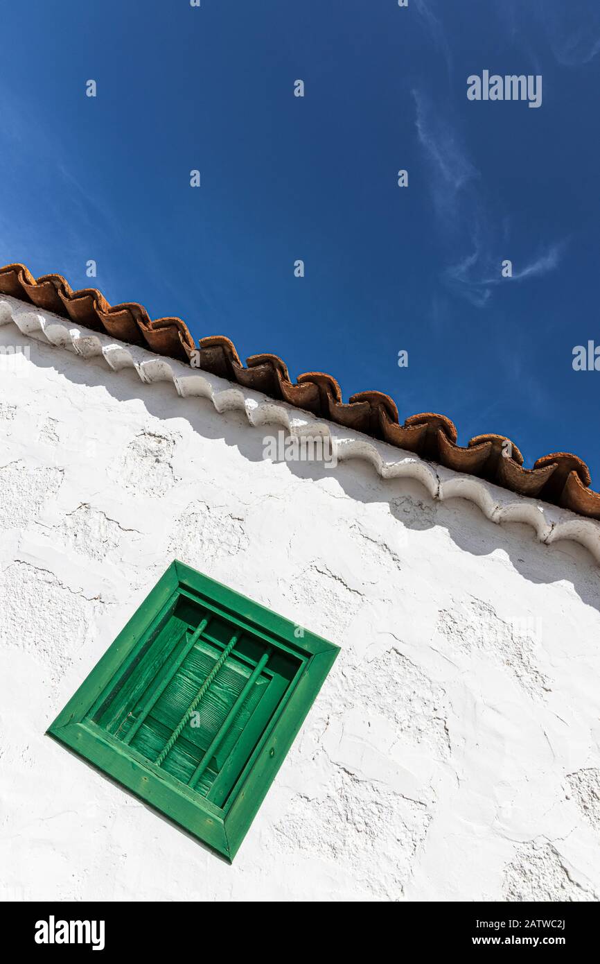 Architettura astratto dettaglio di finestra verde su un muro imbiancato a calce con tetto in terracotta tegole contro un cielo blu su un antico edificio restaurato fattoria, San Foto Stock