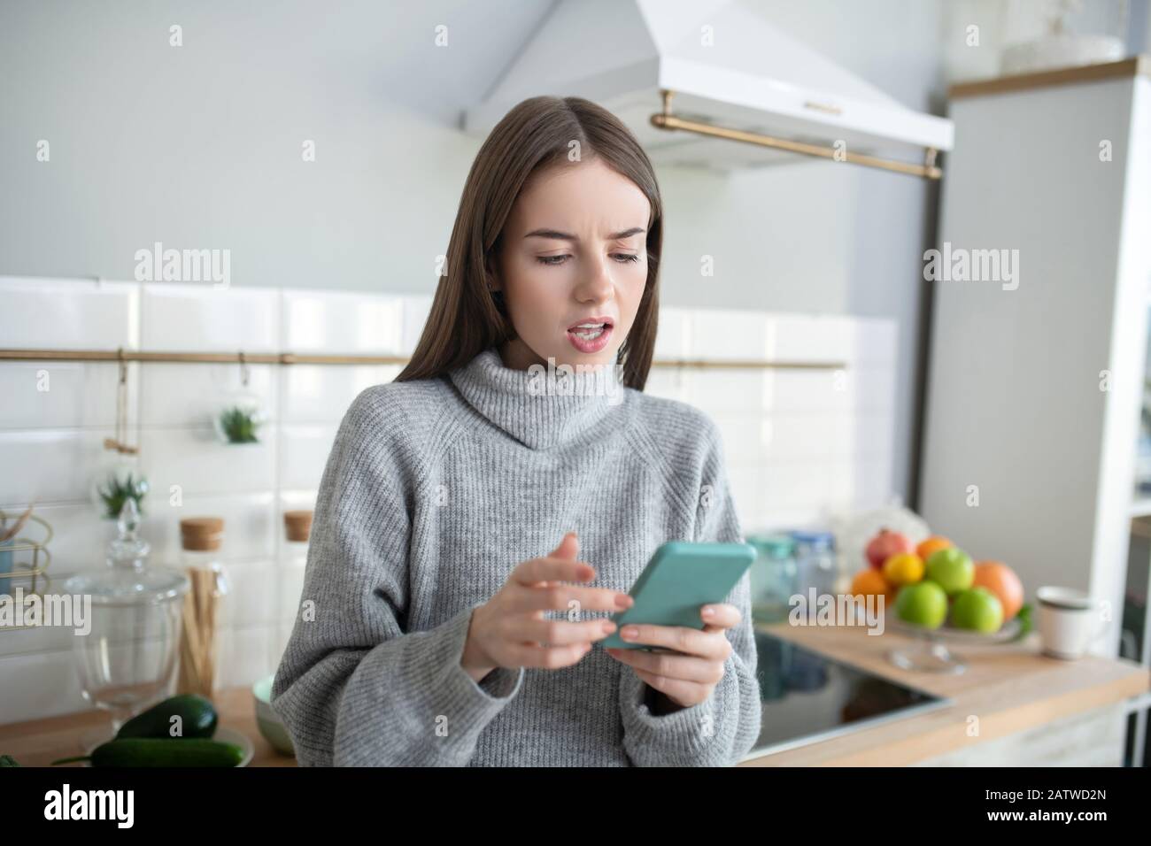Ragazza dai capelli scuri in un maglione grigio che guarda interessato Foto Stock
