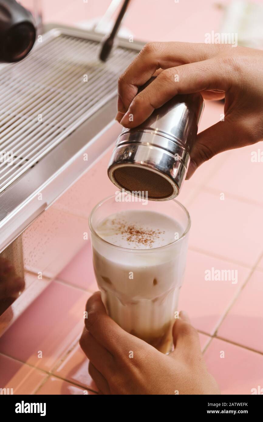 Versare a mano il cioccolato o la polvere di cacao in un bicchiere di latte di ghiaccio Foto Stock
