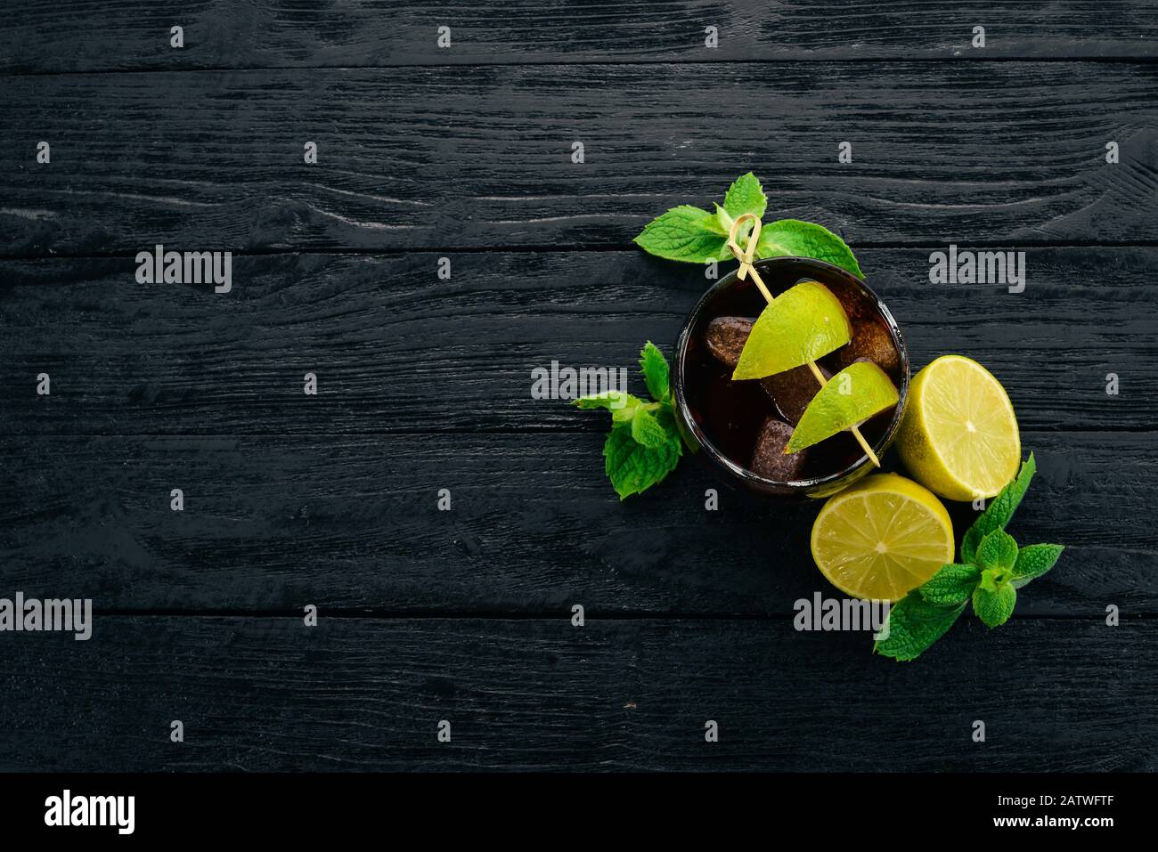 Bicchiere da cocktail Cuba libre. Lime, menta. Su uno sfondo di legno nero. Spazio libero per il testo. Foto Stock