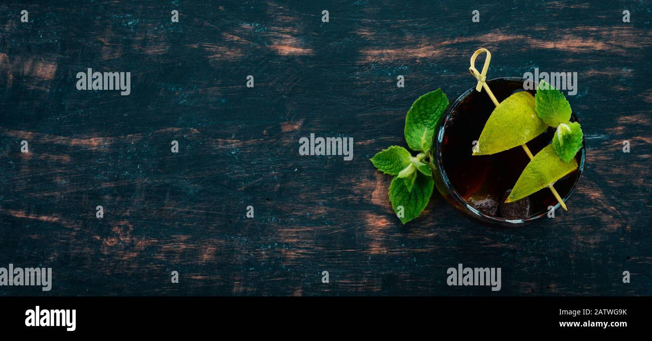 Bicchiere da cocktail Cuba libre. Lime, menta. Su uno sfondo di legno nero. Spazio libero per il testo. Foto Stock