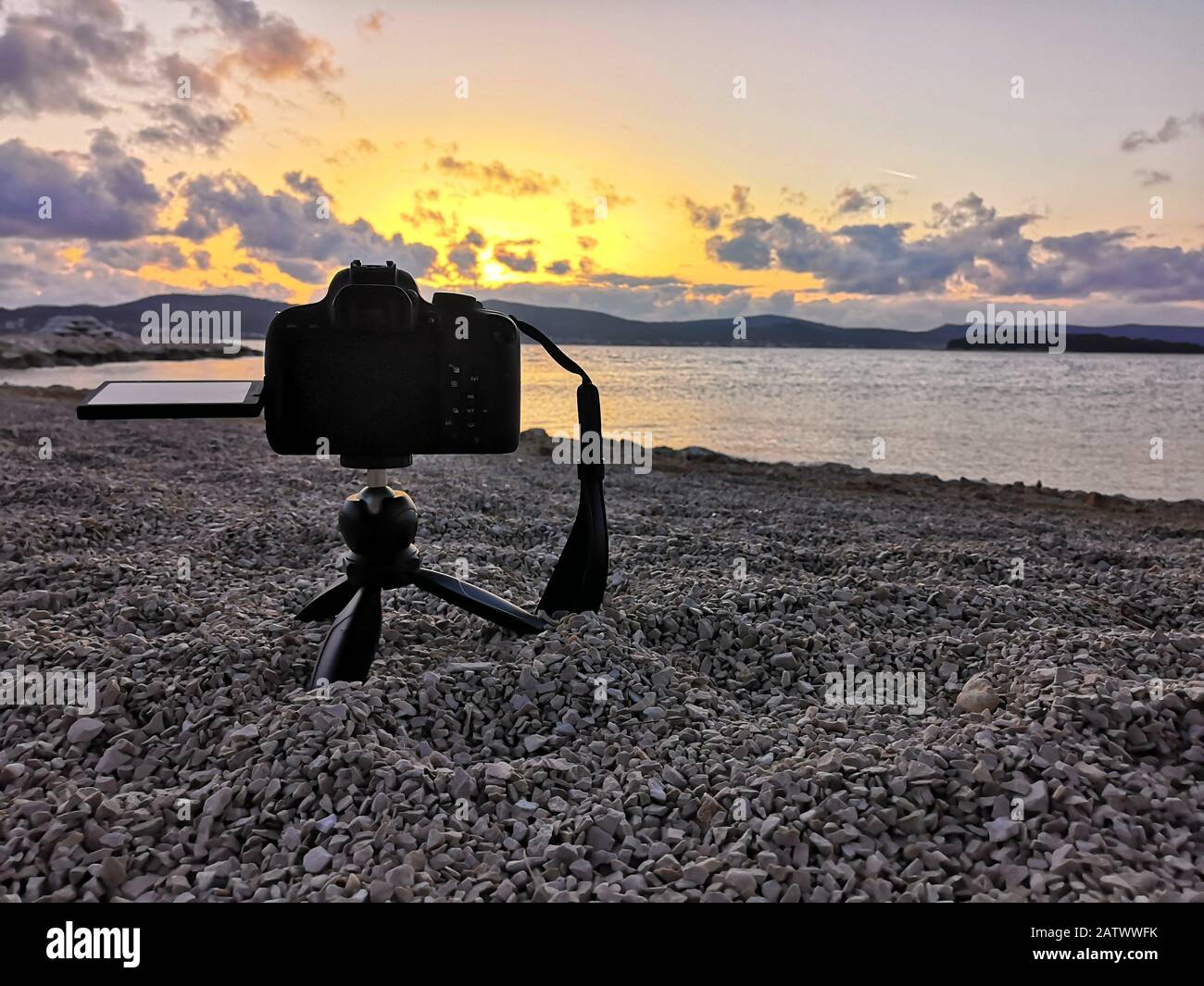 Fotocamera dslr nera su un piccolo treppiede montato sulla spiaggia, filmare e il tramonto in lontananza. Ora oro cielo giallo Foto Stock