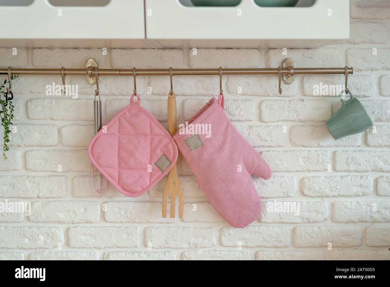 Guanti da cucina, potholder, protezione forno sono appesi su pareti di mattoni bianchi. Concetto di cucina di sicurezza. Spazio di copia Foto Stock
