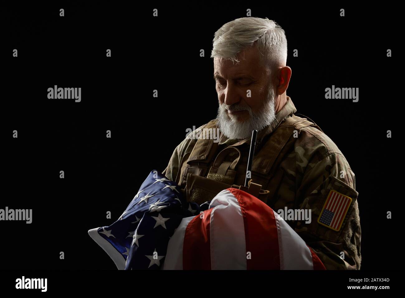 Vista frontale del veterano militare americano con bandiera a braccio. Ritratto di vecchio ufficiale maschile orgoglioso in uniforme camouflage posa in un'atmosfera buia. Concetto di militare, patriottismo. Foto Stock