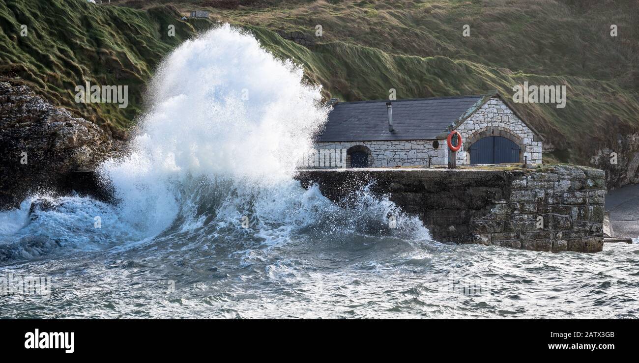 Mari tempestosi che si infrangono contro le mura del porto di pietra che proteggono il boathouse di Ballintoy Foto Stock