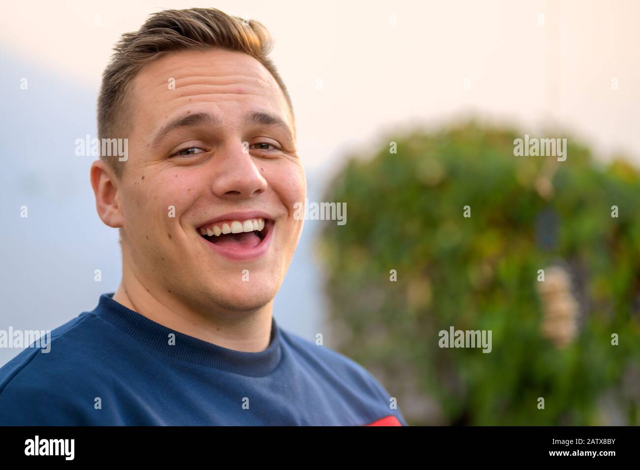 Gioviale attraente giovane uomo ridendo alla macchina fotografica con un'espressione divertito all'aperto in un giardino con spazio di copia Foto Stock