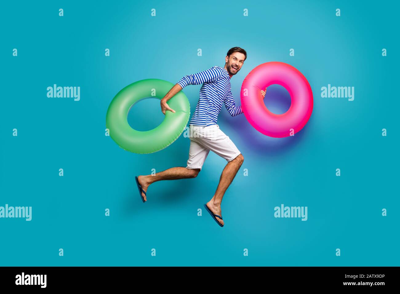 Foto a tutta lunghezza di un pazzo funky turista salto alto corsa nuoto tenere due colorati lifeboe cerchi indossare a strisce sailor camicia shorts flip Foto Stock