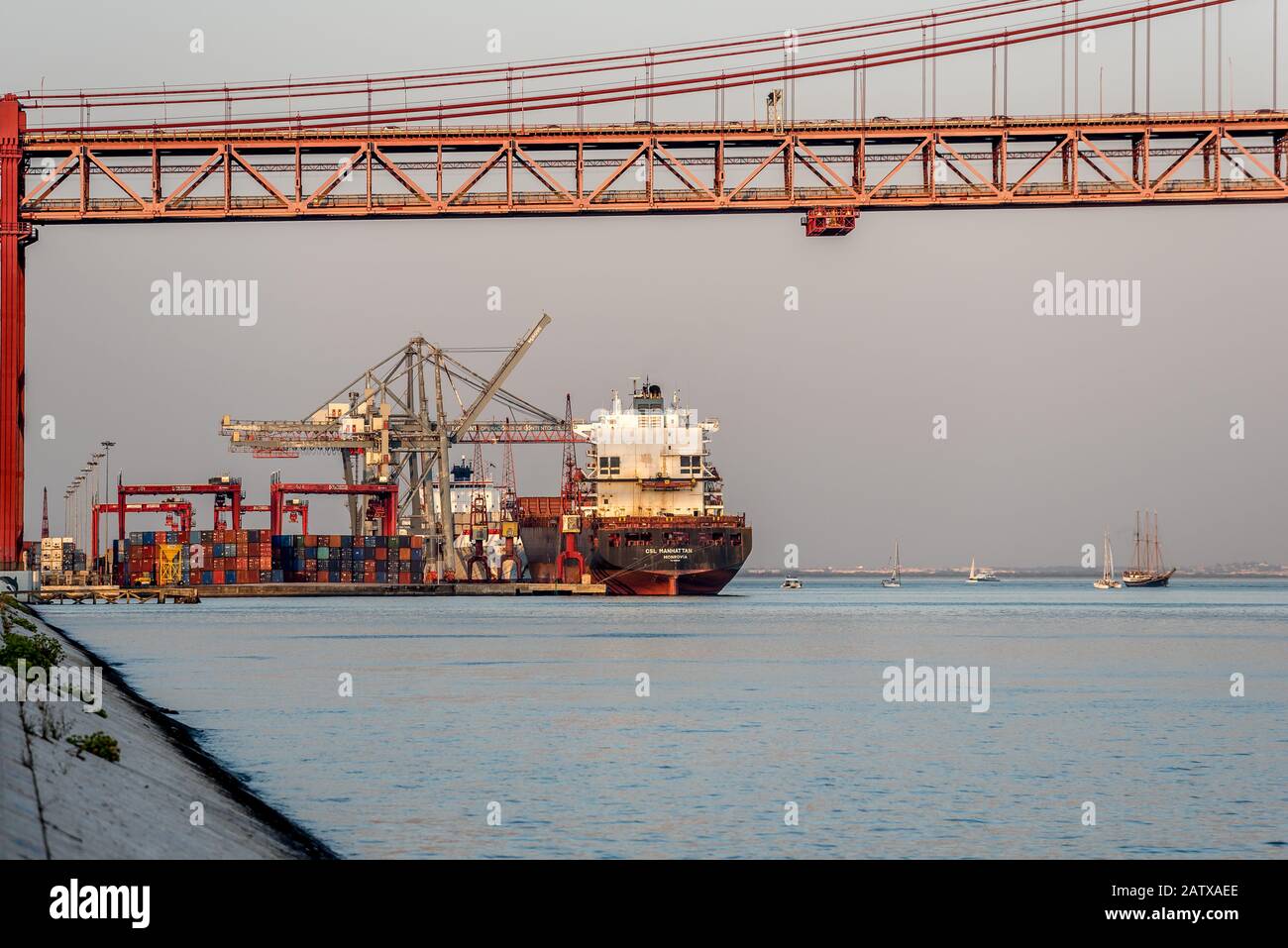 Container nave carico scarico al terminal di spedizione sul fiume Tejo accanto al ponte 25 de Abril in Alcantara Lisbona Portogallo in mare calmo nel pomeriggio Foto Stock