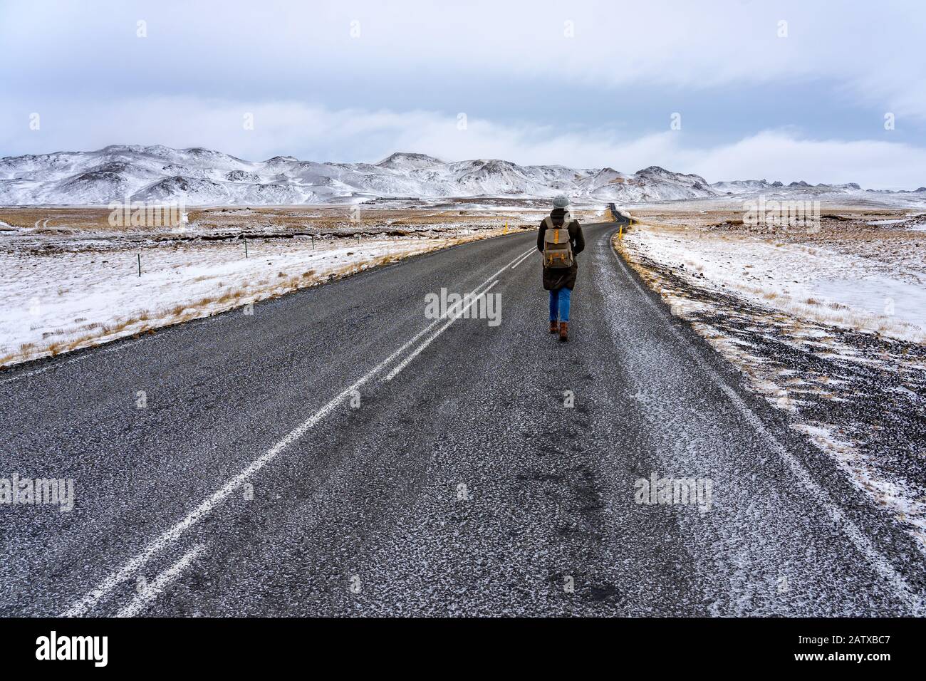Donna che cammina su strada libera di avventura in Islanda inverno tempo con montagne innevate Foto Stock