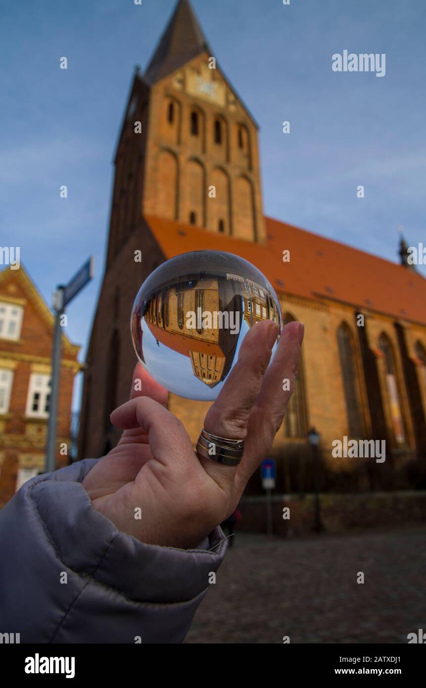 Mano femminile che tiene una palla di vetro in cui è mostrata una chiesa in scala. Magia guardare nel globo di vetro. Vista del mondo in un'altra prospettiva. Foto Stock