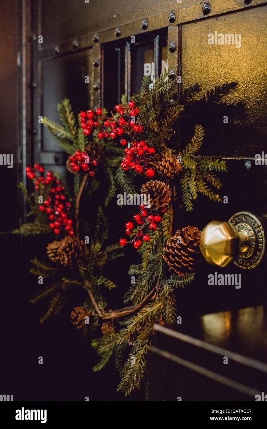 Un giuramento fatto a mano di rami di abete, bacche di oly e coni di pino sulla porta ad un luogo di evento a Natale Foto Stock