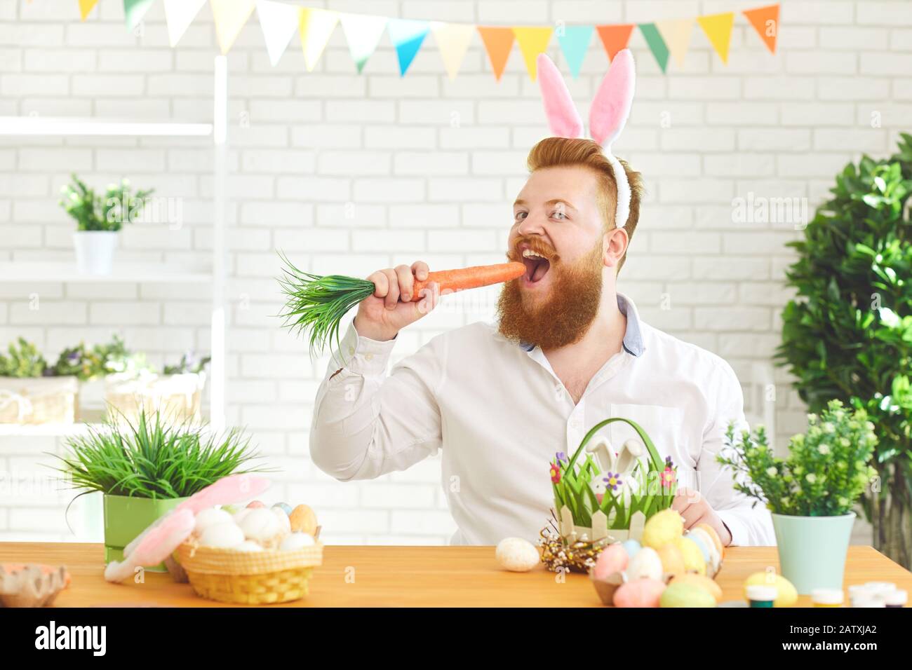 Buona Pasqua. Un uomo grasso sorridente bearded che mangia una carota ad un tavolo con decorazione di Pasqua. Foto Stock