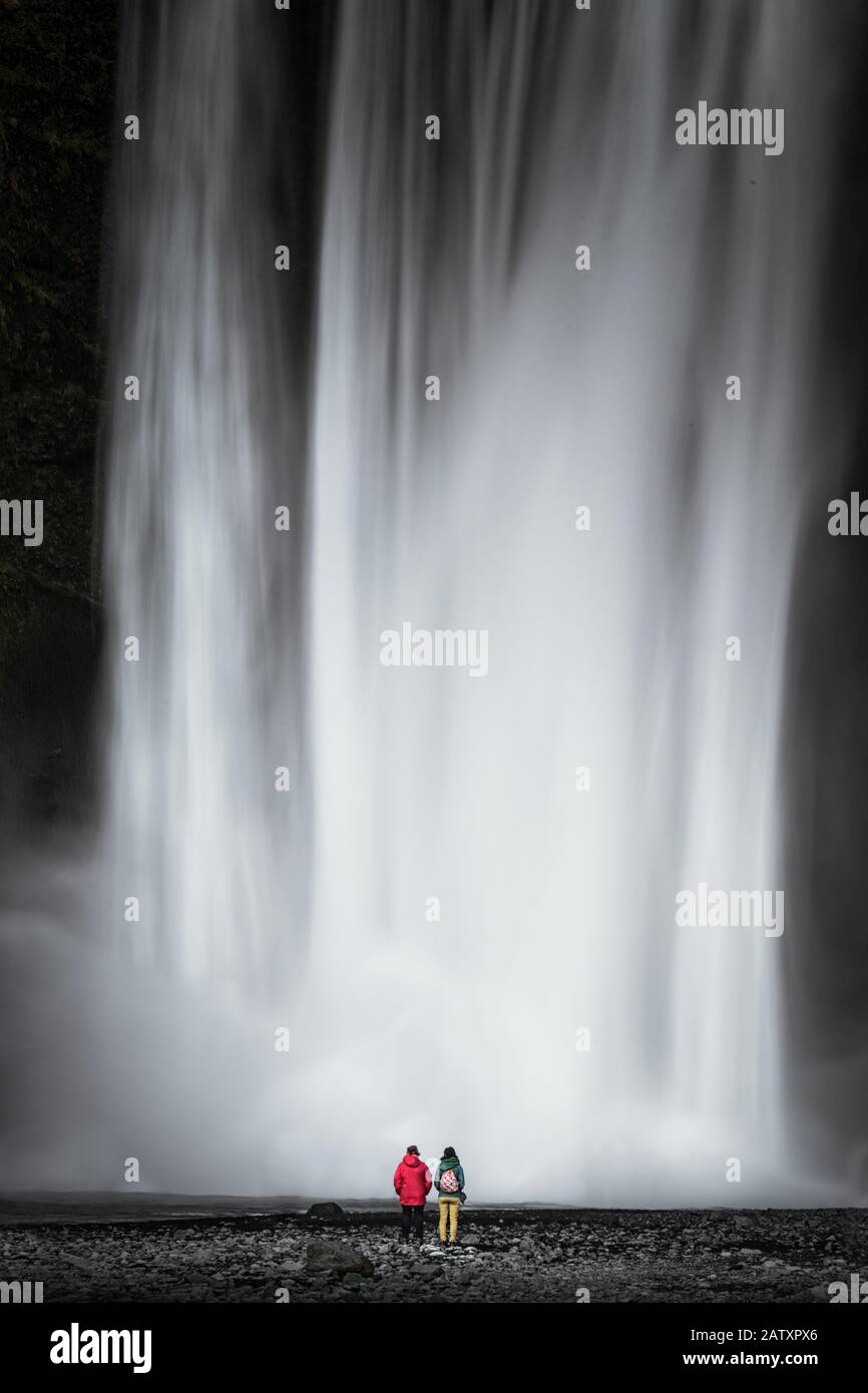 Due turisti si trovano di fronte alla massiccia cascata Skogafoss sulla parte sud dell'Islanda Foto Stock