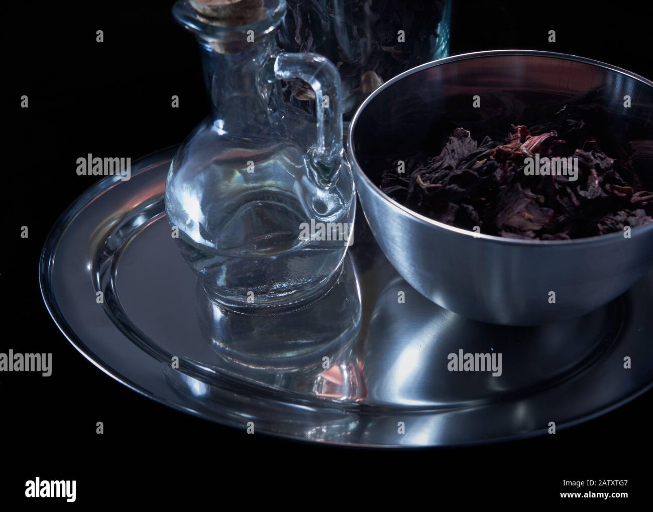 Pewter piatto con una caraffa di vetro semi-riempita e una ciotola di erbe essiccate in un ambiente deliberatamente scuro Foto Stock